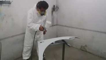 TRABAJADOR REALIZANDO ACTIVIDADES DE PINTURA EN PARTES AUTOMOTRICES, UTILIZANDO TRAJE TIBEK Y MASCARILLA